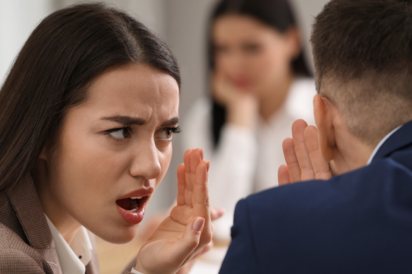 Colleagues gossiping and excluding a female coworker, showing workplace exclusion
